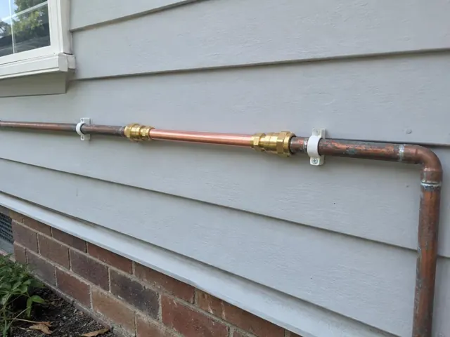 Repaired copper water pipe running along an exterior weatherboard wall in Beverly Hills