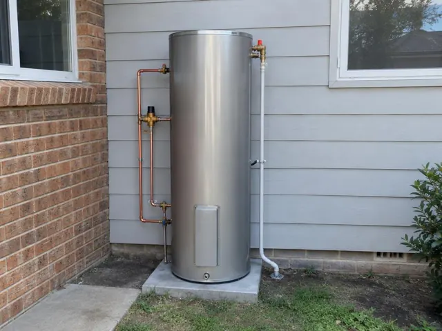 External hot water cylinder beside brick and weatherboard walls with copper and relief piping in Kingsgrove